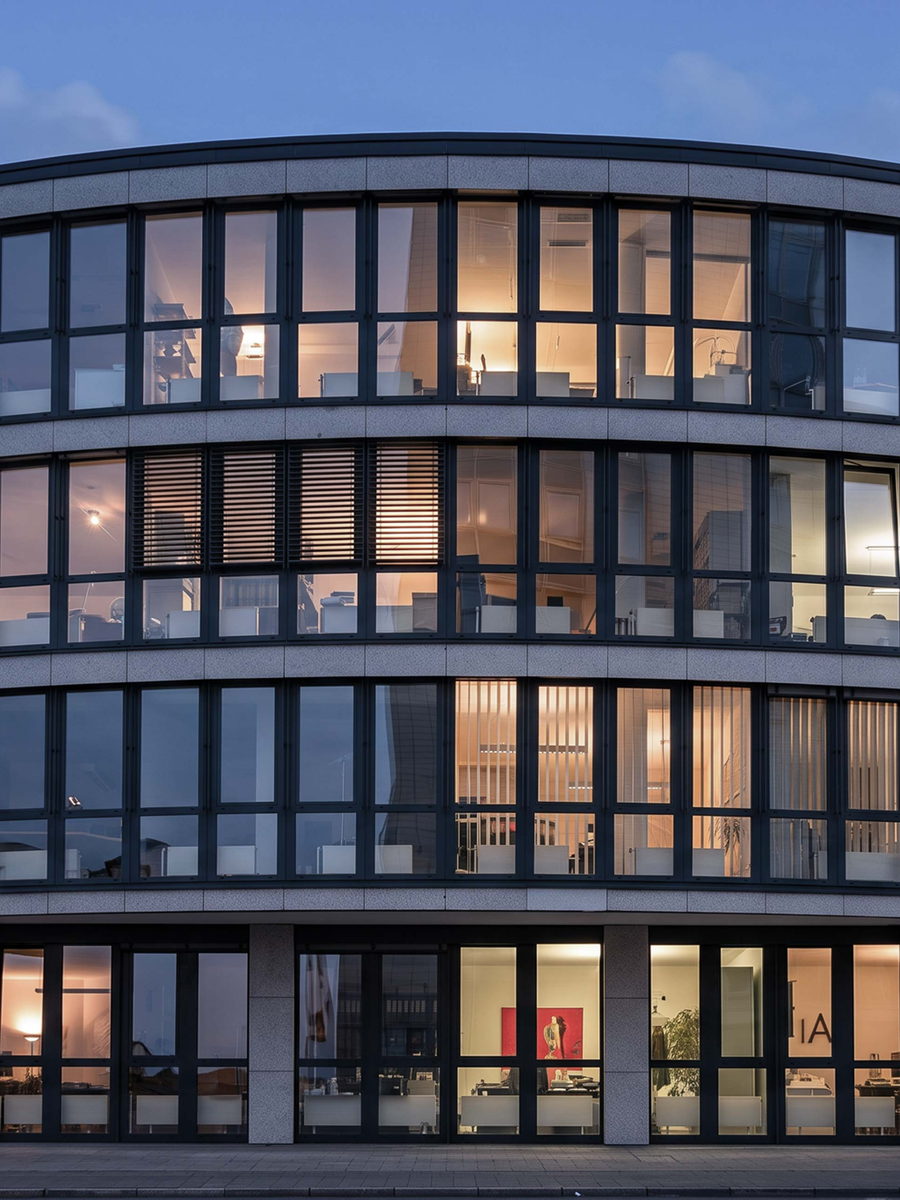 Bürogebäude mit geschwungener Glasfassade und erleuchteten Büros in der Dämmerung – Neugründung einer Unternehmensberatung